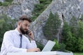 worker guy at desk using computer laptop, phone, looking at screen. Outdoor young hipster having conversation on phone Royalty Free Stock Photo