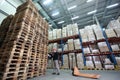 Worker with hand pallet truck at large stack of wooden pallets in storehouse
