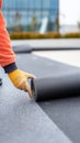 Worker hand in yellow glove unrolling black waterproofing membrane on rooftop. Construction professional installing protective Royalty Free Stock Photo