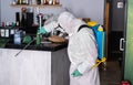 Worker in hazmat suit wearing face mask protection while making disinfection inside bar restaurant - Coronavirus decontamination