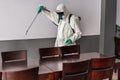 Worker in hazmat suit wearing face mask protection while making disinfection inside bar restaurant - Coronavirus decontamination