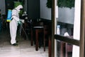 Worker in hazmat suit wearing face mask protection while making disinfection inside bar restaurant - Coronavirus decontamination