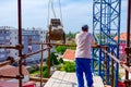 Worker is helping crane to manage wheelbarrow loaded with concrete blocks