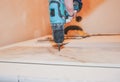 Worker is holding in hands electric drill and cutting panels in apartment. Maintenance repair works renovation in the flat with