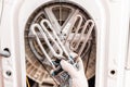 A worker holds a broken and new washing machine heating element. Close up. In the background, the drum of the washing machine