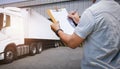 Worker Holds a Clipboard Controlling the Loading of Cargo into Shipping containers. Trucks Parked Loading at Dock Warehouse. Royalty Free Stock Photo