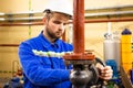 Worker on industrial plant. Technician operator turning gate valve on boiler system. Man in helmet and workwear services refinery Royalty Free Stock Photo