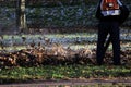 worker with industrial vacuum cleaner collect fallen maple and oak leaves in a heap