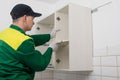 A worker inserts a shelf into the top cabinet of kitchen furniture