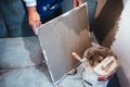 Worker installing bathroom ceramic floor tiles, adding flexible cement adhesive with comb trowel