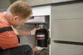 The worker is installing a household waste shredder