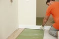 The worker installs plinths in the apartment. Installing a white plastic skirting board on a laminate - adjusting and trimming