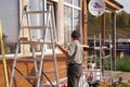 A worker installs scaffolding to repair a wooden house outside on a sunny autumn day