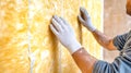 Worker insulates yellow wall with rock wool while using professional tools, showcasing hands and materials in a close-up profile Royalty Free Stock Photo