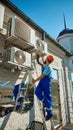 Worker on ladder maintaining multiple air conditioning units on building wall Royalty Free Stock Photo