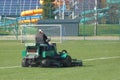 Worker on a large green lawn mower mows the grass on the football field. Landscape design and maintenance of green areas of the Royalty Free Stock Photo