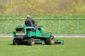 Worker on a large green lawn mower mows the grass on the football field. Landscape design and maintenance of green areas of the