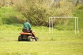 Worker on a large green lawn mower mows the grass on the football field. Landscape design and maintenance of green areas of the Royalty Free Stock Photo