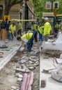 Worker laying interlocking pavers during sidewalk construction with raised soil full of pipes and pipes to be laid