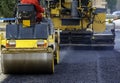 Worker leads the vibrating road roller to compact the asphalt