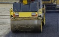 Worker leads the vibrating road roller to compact the asphalt laid out for the construction of a road