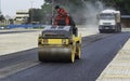 Worker leads the vibrating road roller to compact the asphalt