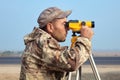 Worker with level, surveyor builder with geodesy equipment close to highway, with mobile phone, smiling.