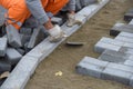 A worker levels the sand, laying paving slabs.