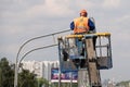 Worker in lift bucket during installation of metal pole with street lamp, street light pole with double head