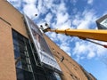 Worker on lift hanging up giant advertising poster on mall building.