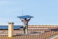 A worker lifts a solar panel on the top of a red-tiled roof to install a photovoltaic system Royalty Free Stock Photo