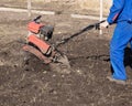 Worker with a machine cultivator digs the soil in the garden