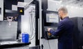 Worker man entering data in CNC drill machine at automatic factory floor. Modern process metal detail production going