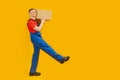 Worker man holding delivery courier box and taking step, goods delivery. Studio photo on yellow background. Copy space, mock up