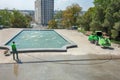 Worker man in uniform washes street or park sidewalk near water pool or fountain. Municipal service of city cleaning process. Guy