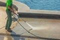 Worker man in uniform washes street or park sidewalk near water pool or fountain. Municipal service of city cleaning process. Guy