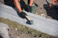 A worker knocks a hammer on the curb, sets blocks in the cement.