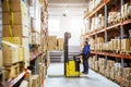 Worker Moves Cardboard Boxes using Hand Pallet Truck, Walking between Rows of Shelves with Goods in Cardboard Boxes in