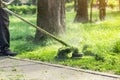 Worker mowing tall grass with electric or petrol lawn trimmer in city park or backyard. Gardening care tools and equipment. Royalty Free Stock Photo