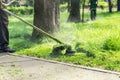 Worker mowing tall grass with electric or petrol lawn trimmer in city park or backyard. Gardening care tools and equipment. Royalty Free Stock Photo