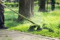 Worker mowing tall grass with electric or petrol lawn trimmer in city park or backyard. Gardening care tools and equipment. Royalty Free Stock Photo