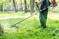 Worker mowing tall grass with electric or petrol lawn trimmer in city park or backyard. Gardening care tools and equipment. Royalty Free Stock Photo