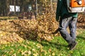 Worker operating heavy duty leaf blower in city park. Removing fallen leaves in autumn. Leaves swirling up. Foliage Royalty Free Stock Photo