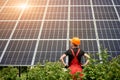 Worker in orange uniform stands with his back to camera against the background of large plantation solar batteries Royalty Free Stock Photo