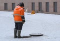 A worker in an orange uniform stands over an open sewer