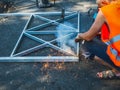 A worker in an orange vest welds a metal fence on freshly paved asphalt