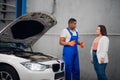 Worker in uniform shows the client the engine of a car