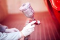 Worker painting a red car in painting booth using spray gun