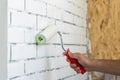 A worker paints a brick wall with white paint using a paint roller