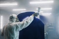 Worker paints car body part in workshop chamber using airbrush. Man using spray gun during auto painting. Royalty Free Stock Photo
